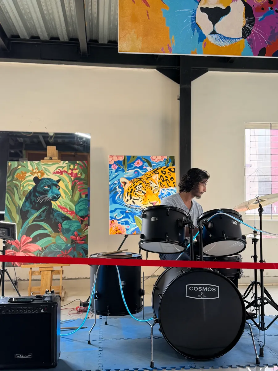 Close view of the drummer mid-song behind the toms and cymbal, framed by the panther and jaguar paintings propped along the studio wall.