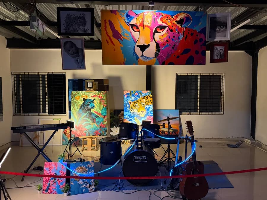 The studio at night from further back - barred windows on either side, a gallery wall of animal paintings above, and the keyboard, drum kit and acoustic guitar arranged along a floor mat lit by blue LED rope light.