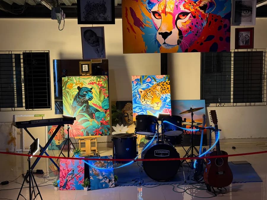 Canvases grouped together at night: a black panther among jungle foliage, a jaguar swimming in blue water, a gilded Buddha with a white lotus, and cherry-blossom bird paintings propped on the floor beside the drum kit.