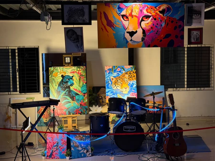 The night display head-on - the panther canvas on its wooden easel next to a Casio keyboard, the drum kit ringed in blue light, and an acoustic guitar leaning at the right beneath the big cheetah painting.